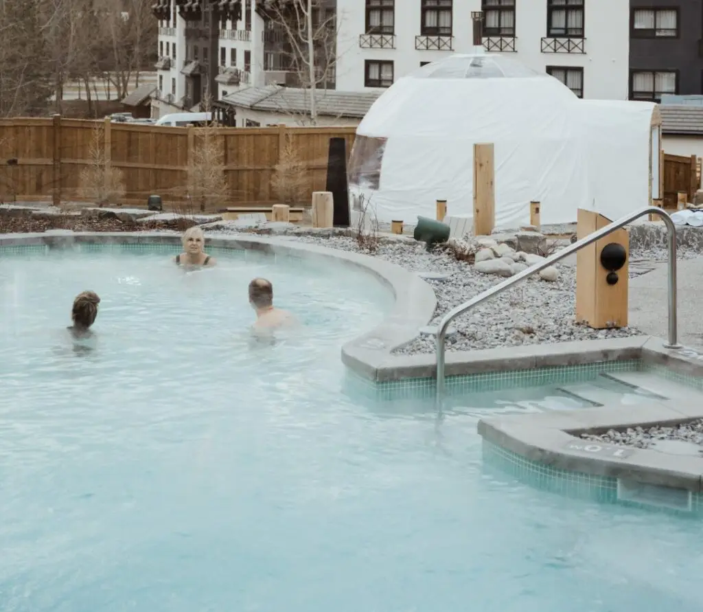 People relaxing in a steaming hot pool at The Rise, with a geodesic dome in the background.