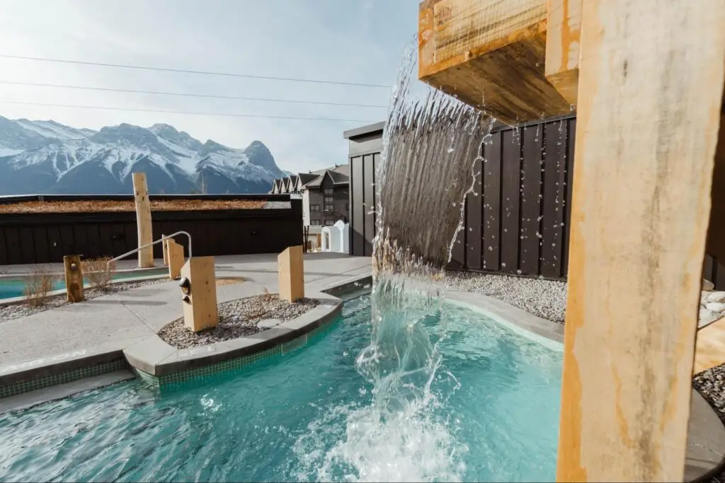 Cold plunge pool with waterfall and mountain backdrop, promoting sleep benefits.