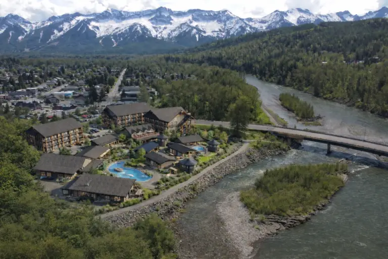 Aerial view of a resort complex near snow-capped mountains and a river.