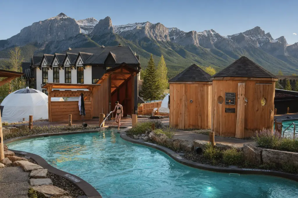 Woman in bikini uses pool net in outdoor spa with mountains