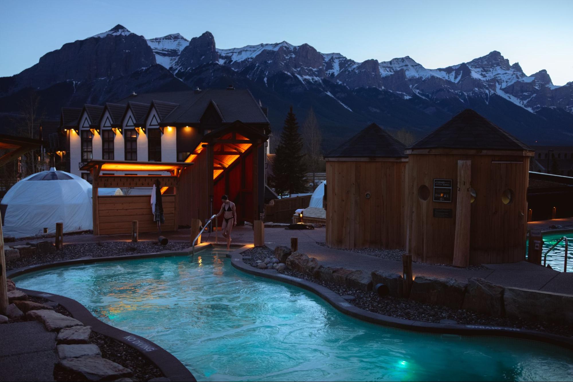 Woman entering hot springs pool at dusk with snowy mountains behind
